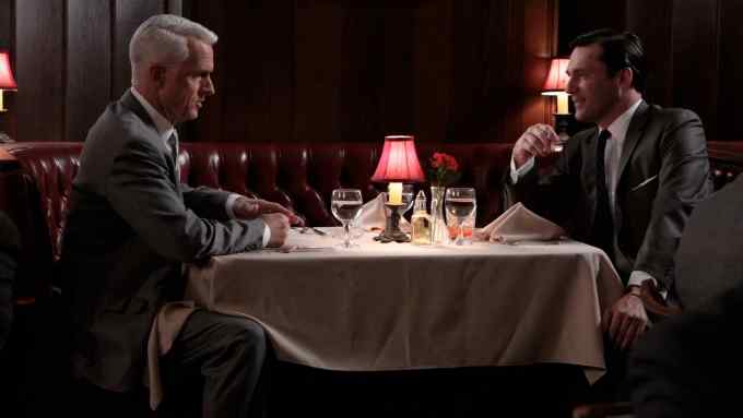 Two businessmen facing each other across a restaurant table in a scene from the TV series ‘Mad Men’