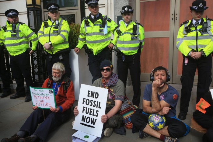 Extinction Rebellion protestors sit in front of a cordon of police outside BP’s offices in London