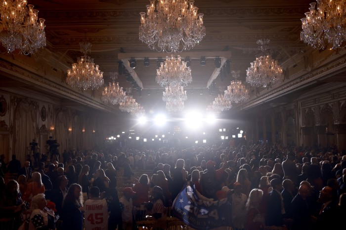 The Grand Ballroom at Mar-a-Largo. Huge chandeliers hang from the ornate ceiling and the room is full of Donald Trump supporters, waiting for him to announce he is running again