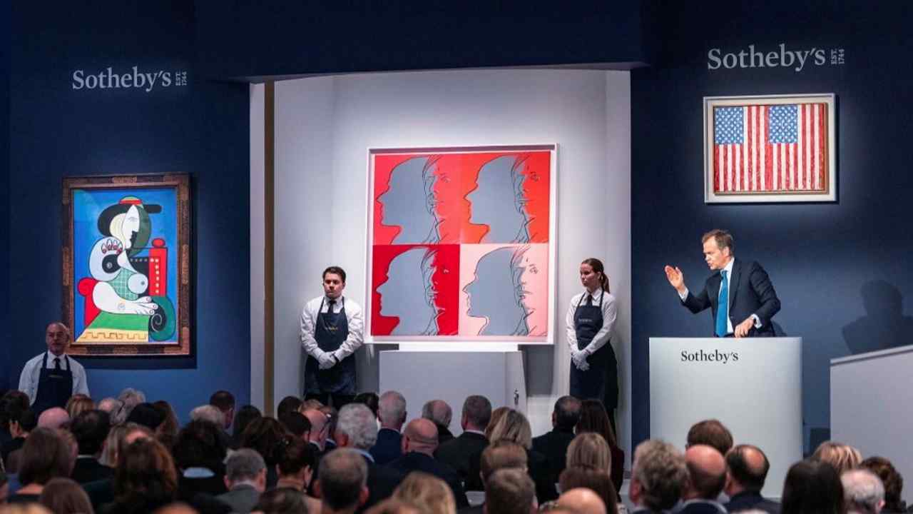 A crowd watch an auctioneer as he tempts bids for modernist paintings