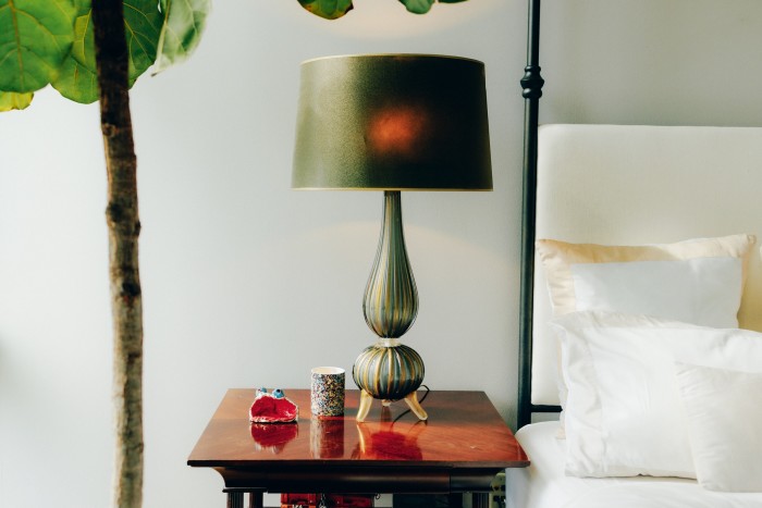 Meja sisi katilnya, dengan salah satu daripada sepasang lampu Murano vintaj ditemui di pasar lambak Paris, serta karya seni anaknya
