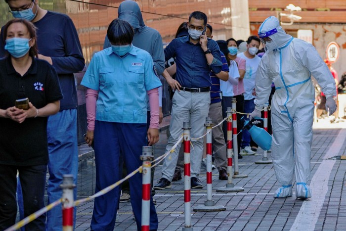 A worker in a protective suit sprays disinfectant past a line of residents waiting for Covid-19 testing.