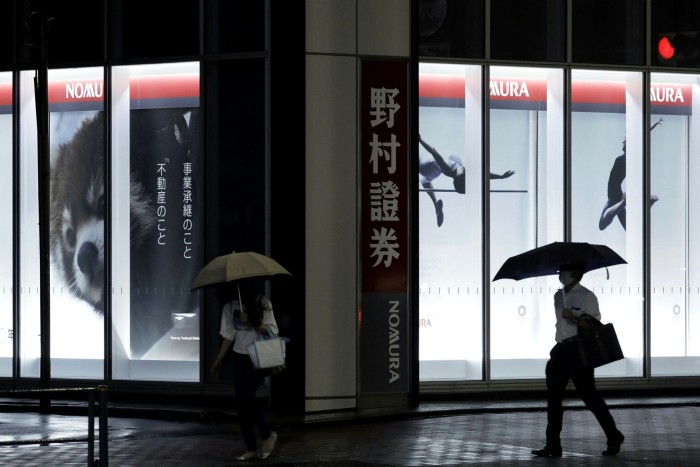 People walk past the offices of Nomura in Tokyo, Japan