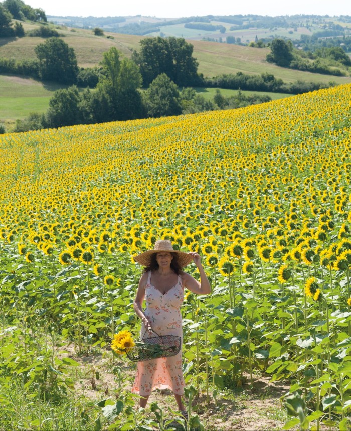 Kathryn M Ireland wearing a hat and sundress in a sunny field of sunflowers