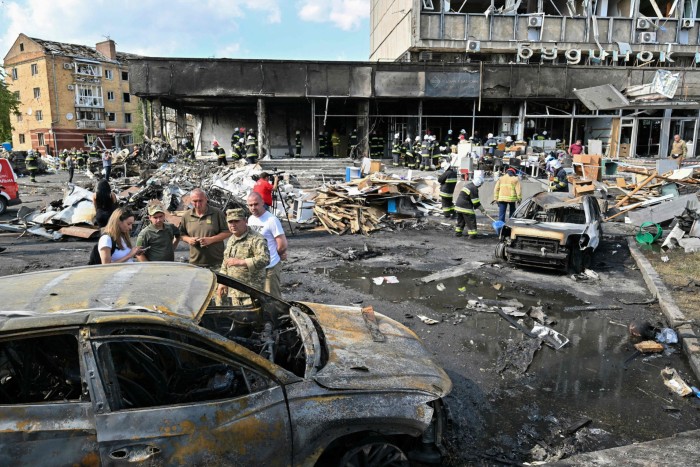 Firefighters sift through burnt wreckage and cars outside a bombed building