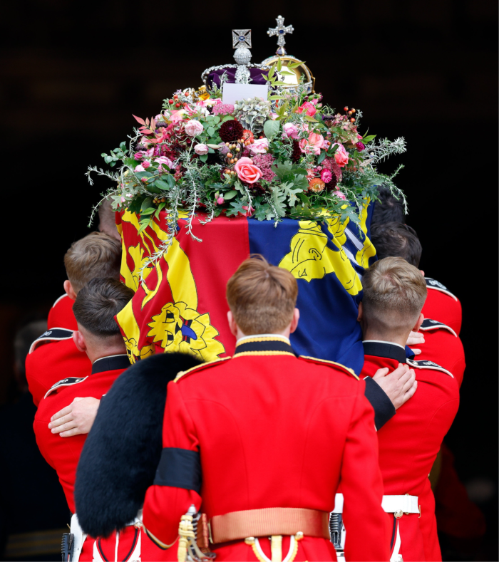The bearer party of eight soldiers in red uniform carry the late Queen’s coffin on the shoulders. The coffin is draped in the royal standard and topped by a bouquet of flowers