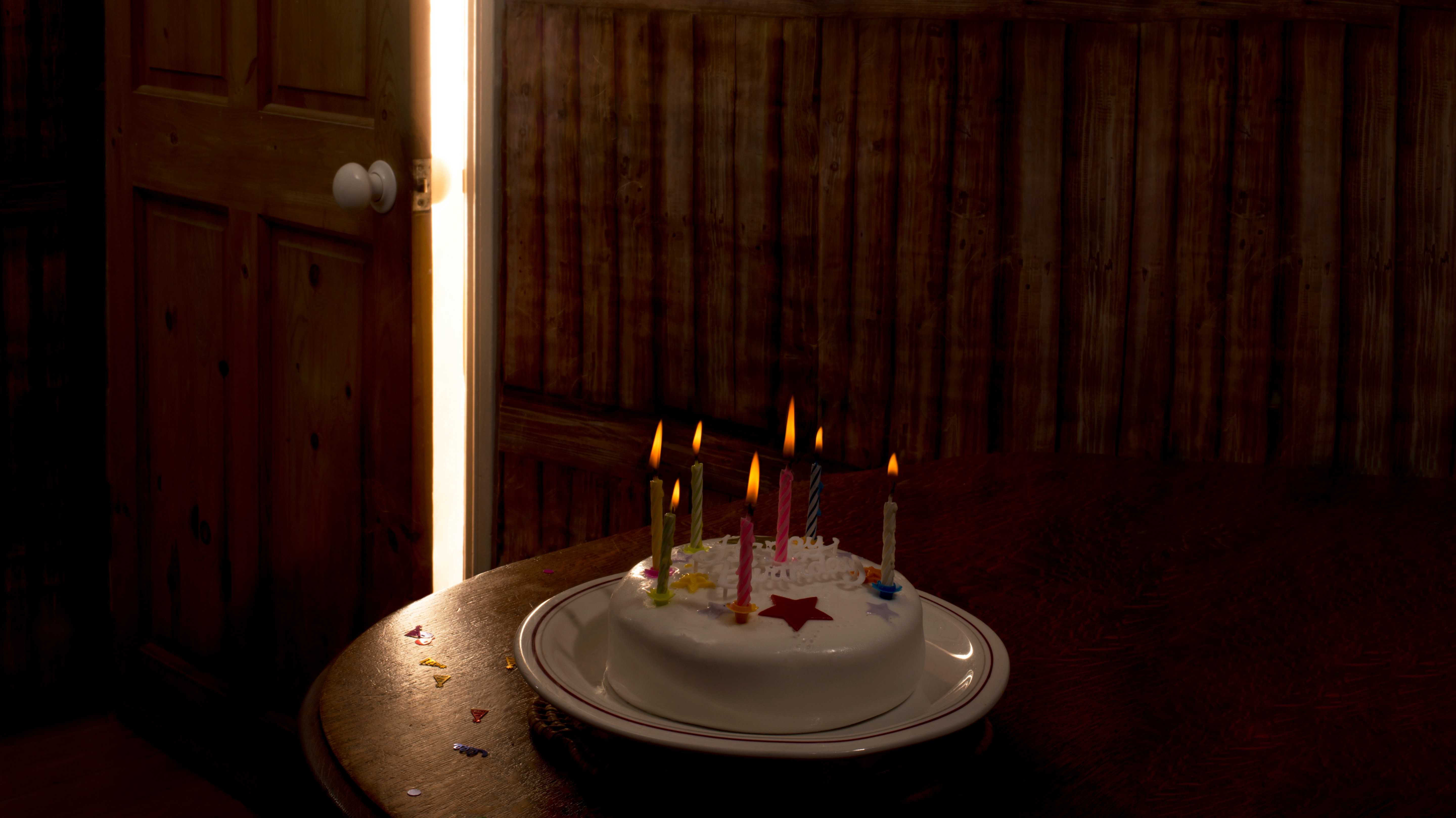 A birthday cake with seven lighted, coloured candles on a wooden table