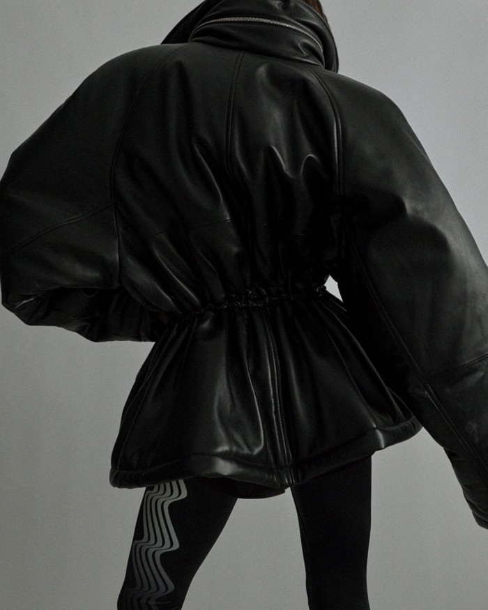 A model, seen from behind, wears a black leather jacket with  oversized shoulders and nipped-in waist