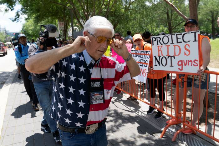 A member of the National Rifle Association plugs his ears with his fingers as he walks past protesters during the NRA's annual meeting in Houston