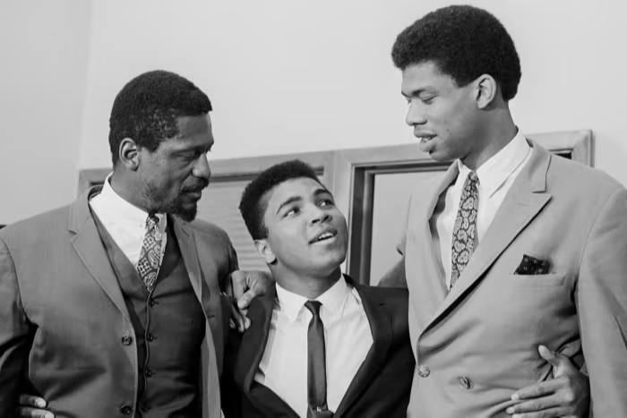 محمدعلی (در آن زمان کاسیوس کلی) توسط راسل، سمت چپ، بازیکن-مربی 6 فوت 11 اینچی بوستون سلتیکس، و ستاره 7 فوت و 3 اینچی دانشگاه، لو آلسیندور (بعدها کریم عبدالجبار)، سمت راست، در سال 1967 کوتوله می شود.