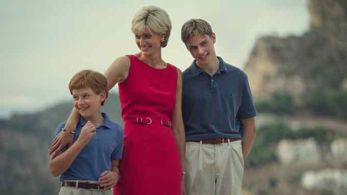 A woman with shortish blond hair in a red dress hugs her two children