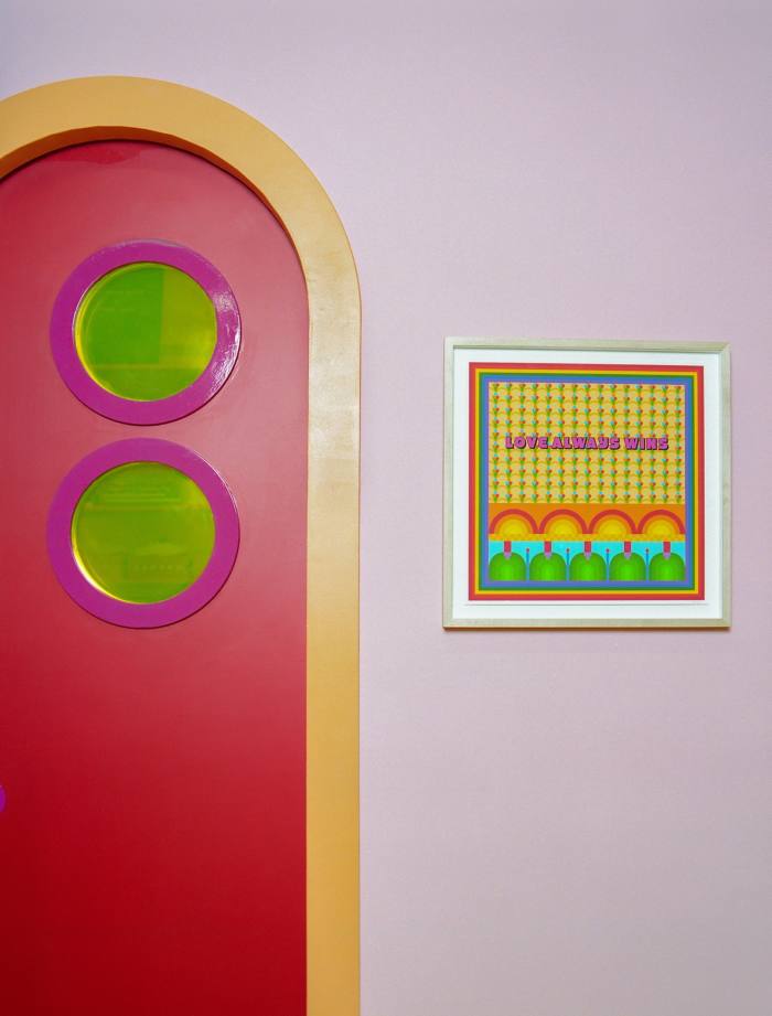 A bright red arched door with a yellow frame in a lilac wall on which hangs a vividly coloured patterned artwork in Yinka Ilori’s studio