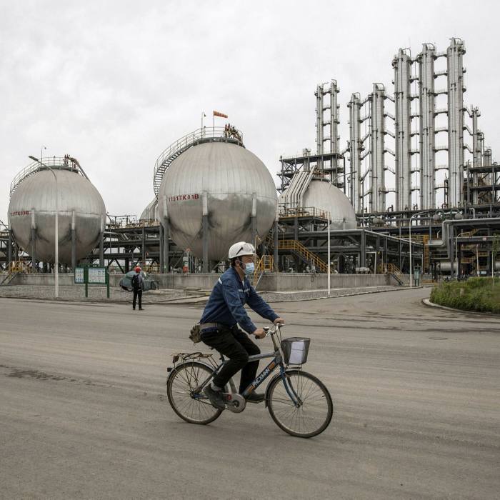 A worker rides a bicycle in front of the storage tank and distillation towers at the Daqo New Energy plant