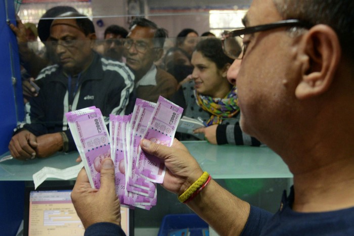 An Indian bank teller counts out notes as senior citizens wait to withdraw money at a bank in Amritsar, India