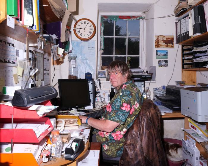 Lindsay Ketteringham, the landlord of the Neuadd Arms at his desk in the pub’s office. Ketteringham is wearing a flowery shirt and is sitting at a computer
