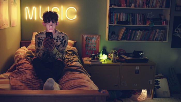 Film still of a boy lounging on his bed looking at telephone screen in ‘Heartstopper’