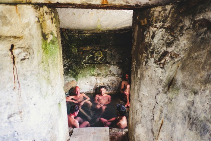 Men bath in hot water in a very basic stone hut