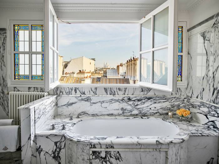 A marble bathroom with a window above offers views of the roofs and a cathedral in the distance