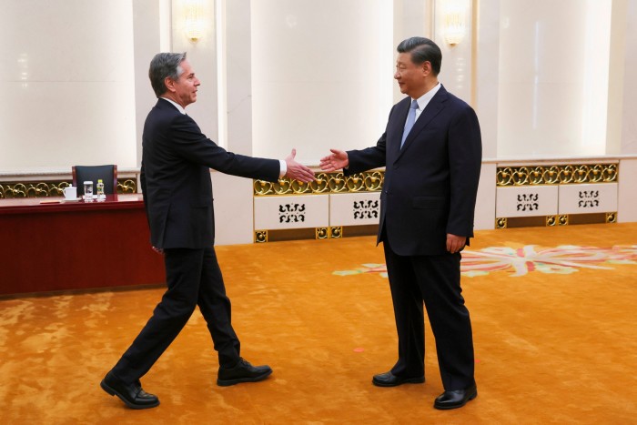 A US official in a dark suit shakes hands with an Asian man in a suit in a large hall