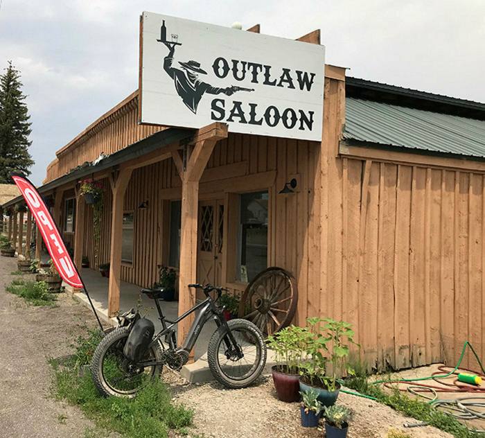 The exterior of the Outlaw Saloon, a timber building in Hatch, Utah. The bar’s sign shows a cowboy with a tray in one hand and a gun in the other
