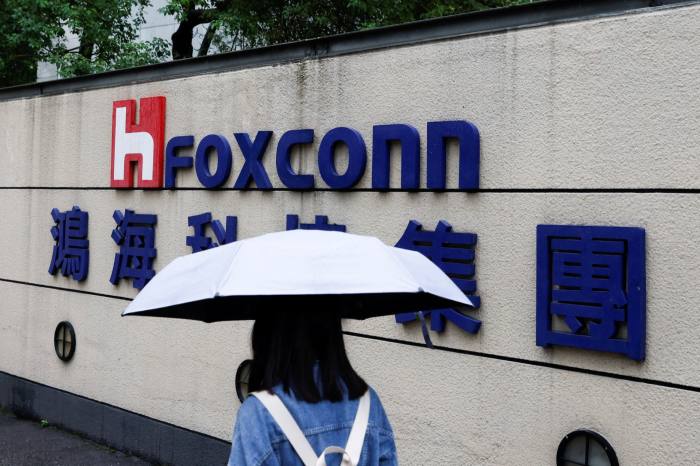 Una mujer con un paraguas pasa junto al logotipo de Foxconn frente a un edificio.
