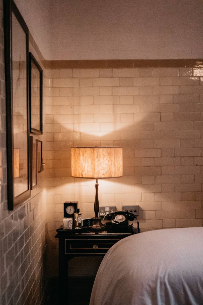 A lamp on a small table in front of original tiles on the wall of the former magistrates’ court in which the NoMad hotel is housed