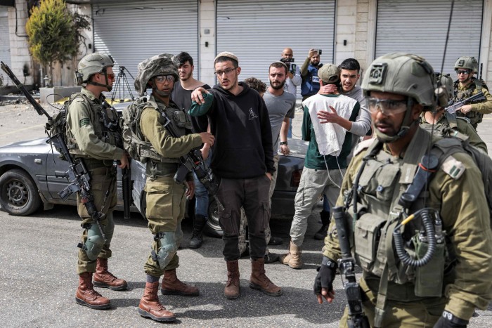 Israeli soldiers speak with Israeli settlers in the town of Huwara near Nablus in the occupied West Bank on Monday following a shooting attack