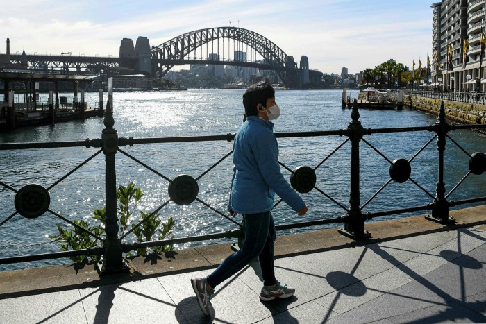 Una signora che indossa una maschera cammina nel tranquillo Circular Quay di Sydney