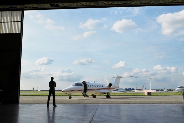 Technician in hangar looking out the doors at a private jet on the tarmac. KKR still does not own any private jets for the use of its executives. But some KKR executives own their own aircraft