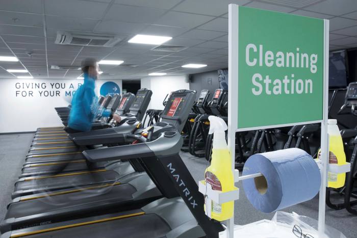 A cleaning station stands as an employee tests a treadmill at a Pure Gym Group health club