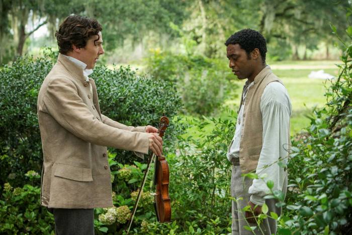 A white man holds out a violin to a black man