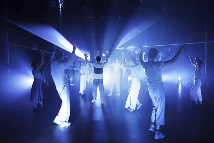 People in casual clothes raise their arms in spotlights in a dark room