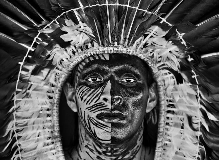 Adão Yawanawá, mirando directamente a la cámara, usa maquillaje y un tocado de plumas de águila, Pueblo de Nova Esperança, Territorio Indígena de Rio Gregório, Estado de Acre, Brasil, 2016
