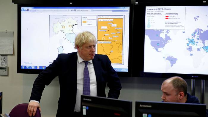 Boris Johnson stands in front of two big screens displaying the early spread of Covid infections in March 2020