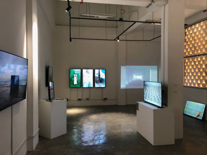 Los monitores de computadora en una galería semioscura muestran imágenes del mar, paredes de azulejos, edificios vacíos
