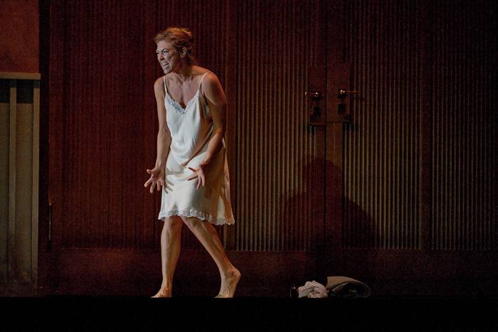 A woman in a white negligee walks a stage and looks anxious