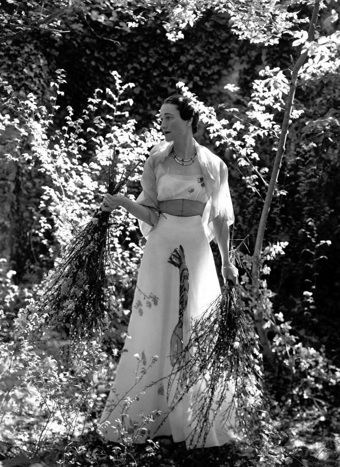 The Duchess of Windsor stands among the foliage wearing a dress decorated with a painted lobster