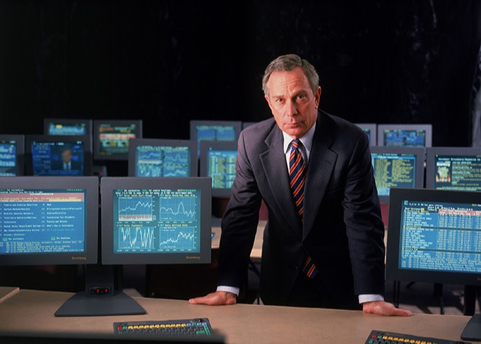 Bloomberg’s founder Michael Bloomberg, in 1998, leaning on a big desk in the training room of his offices in New York. He is surrounded by keyboards and Bloomberg terminals displaying financial information 