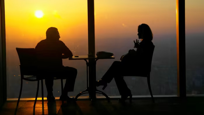 A man and a woman sitting in a room with a sunset behind them