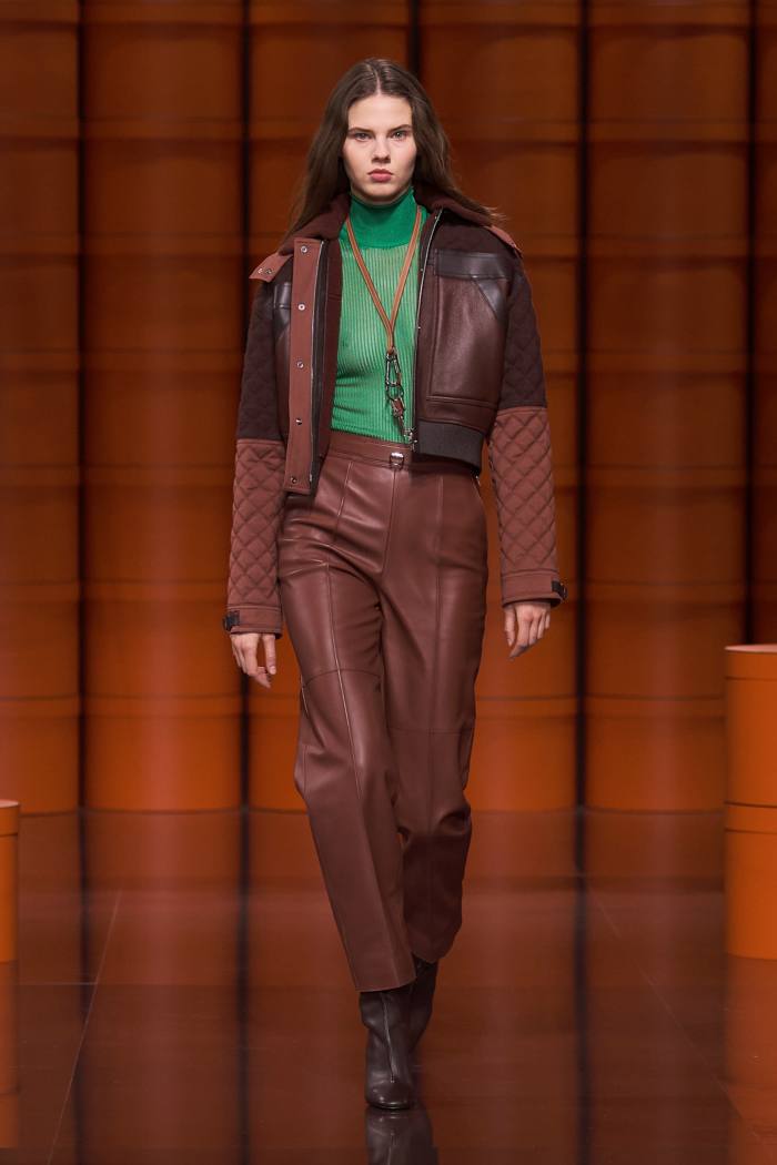 Hermès lambskin short zipped jacket, juniper-green knit funnel-neck jumper, glossy lambskin high-waisted trousers, Swift calfskin, gold and palladium-finish metal wrist strap, and calfskin ankle boots from the house’s AW21/22 collection