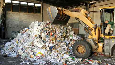 Excavator dumps cardboard garbage at waste recycling plant