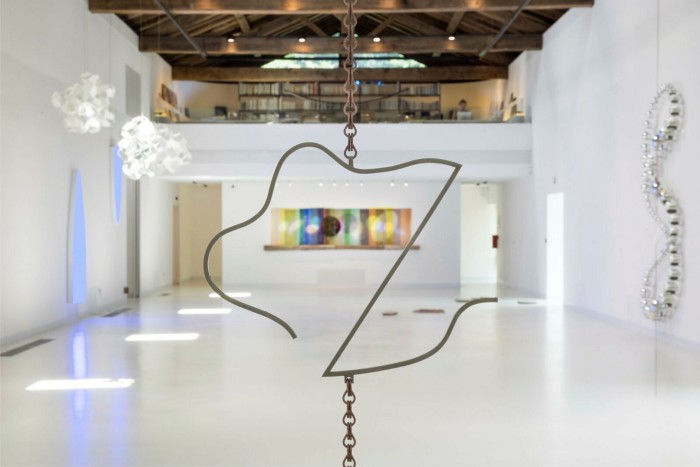 A simple sculpture made from metal wire hangs in a gallery