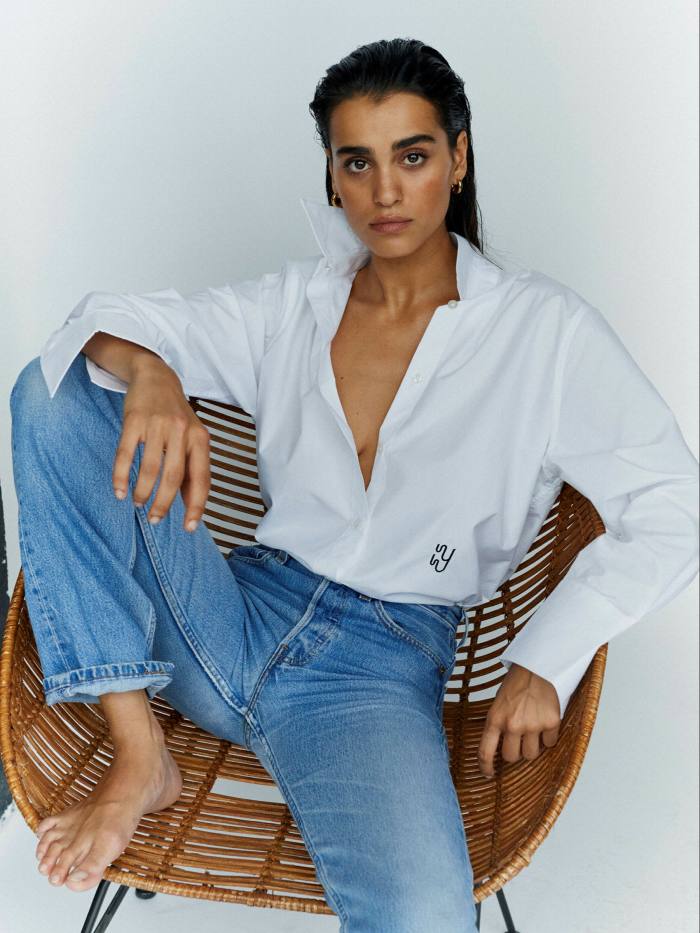 A woman is sitting in a wicker chair.she wears a white shirt and jeans