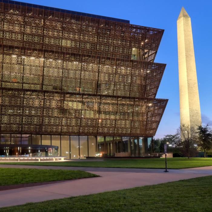 The outside of the three-tiered National Museum of African American History and Culture with the obelisk of the Washington Memorial to the right