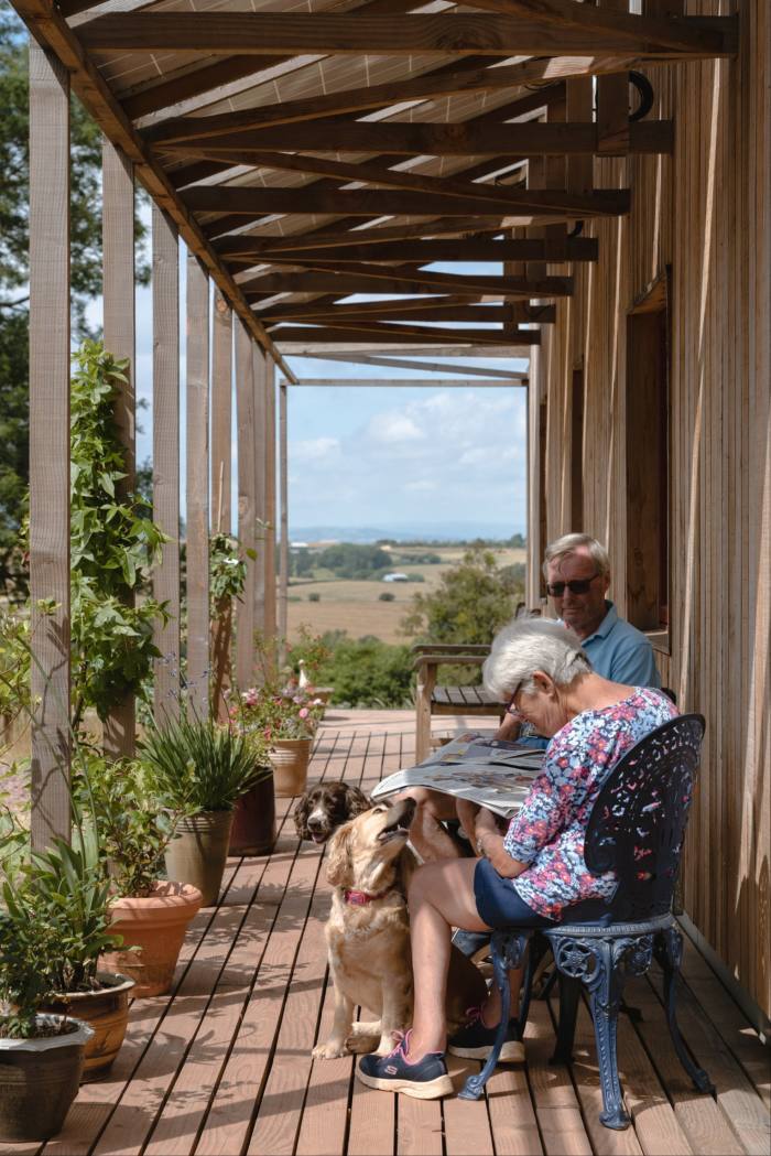 A couple sitting on the shaded front patio of a wooden home