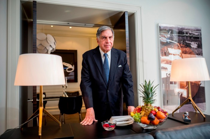 Ratan Tata in a suit and tie leans on a desk in a plush apartment