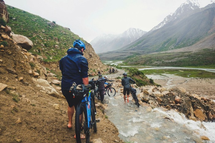 Cycles push their bikes through a muddy stream