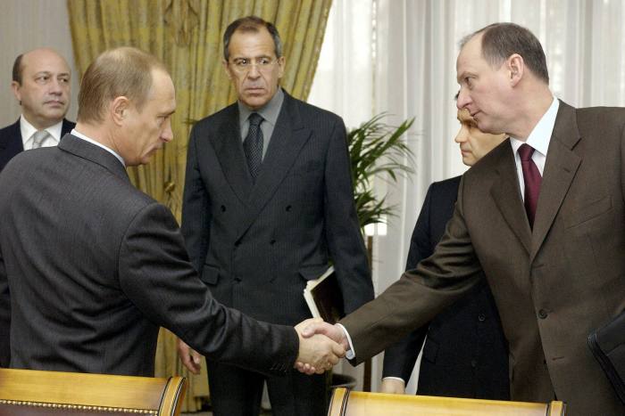 Putin shakes hands with one of his security chiefs as other men in suits look on