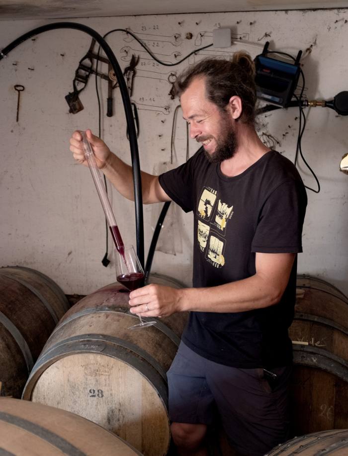 Romain Verger, winemaker at Lé Thio Noots, pours wine from a pipette into a glass in his winery