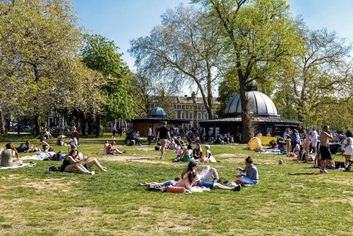 People sitting on the grass in the sun outside the Pavilion Cafe in Victoria Park in east London